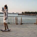 Cheerful young man with boombox riding skateboard