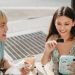 Crop smiling Asian man with cheerful ethnic girlfriend with photo camera at cafeteria table with takeaway coffee