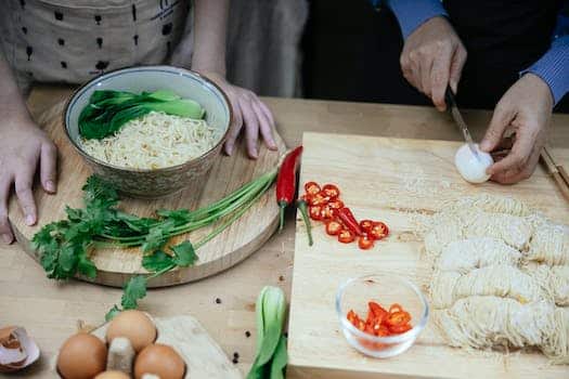 From above anonymous females cutting boiled eggs on wooden cutting board while cooking traditional Asian noodle soup in kitchen