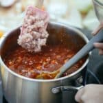 From above of anonymous cook adding minced meat into pan with boiling chili while standing near stove on blurred background