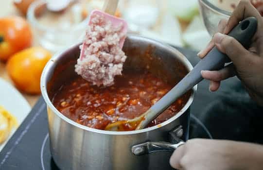 From above of anonymous cook adding minced meat into pan with boiling chili while standing near stove on blurred background