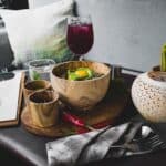 From above of arranged oriental food in wooden dishes on cutting board served with drinks and candle and cutlery and cafe menu on table against comfortable sofa