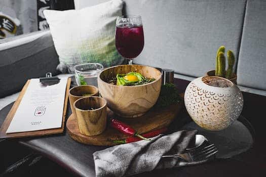 From above of arranged oriental food in wooden dishes on cutting board served with drinks and candle and cutlery and cafe menu on table against comfortable sofa