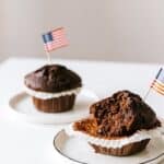 From above of bitten and whole festive chocolate cupcakes decorated with miniature american flags and placed on white table