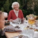 Smiling elderly woman with family and friends enjoying dinner at table backyard garden