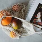 Top view of opened recipe book at table together with handbag with assorted fruits inside