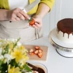 Woman cutting strawberry for decoration of cake