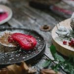 Appetizing composition of freshly baked sweet pie served on black plate with red marinated pear and decorated with sugar powder