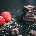 Close-Up Photo Of Stacked Chocolates Bars Beside Raspberries