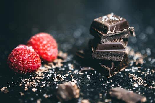 Close-Up Photo Of Stacked Chocolates Bars Beside Raspberries