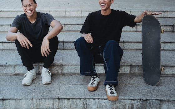 Crop cheerful Asian male friends resting on street steps