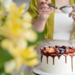 Crop female baker strewing powdered sugar to decorated cake