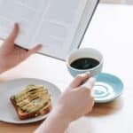 Crop person with cup of americano and book