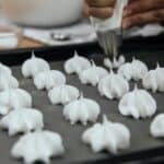 Crop unrecognizable chef with piping bag with star tip forming vanilla meringue cookies on baking pan in kitchen