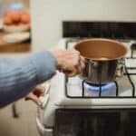 Crop unrecognizable housewife placing saucepan on burning stove