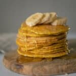 Delicious homemade pancakes covered with honey with sliced bananas placed on wooden chopping board on table in light place