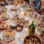 From above crop people enjoying festive dinner with snacks at garden table with candles burning