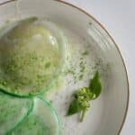 From above of delicious poached egg decorated with green seasoning and herb with leaves on white plate on table