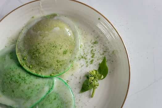 From above of delicious poached egg decorated with green seasoning and herb with leaves on white plate on table