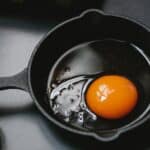 From above of frying pan with uncooked egg yolk and white placed on table near scattered shells in kitchen