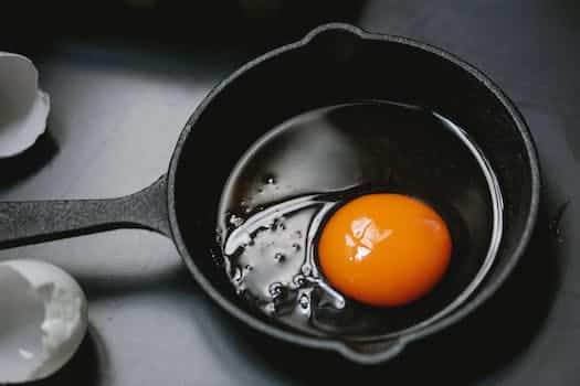 From above of frying pan with uncooked egg yolk and white placed on table near scattered shells in kitchen