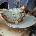 High angle of crop anonymous women transferring uncooked yummy homemade pizza on platter during preparation to baking in kitchen