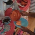 High angle side view of unrecognizable ethnic kid using plastic kitchenware while playing on kitchen