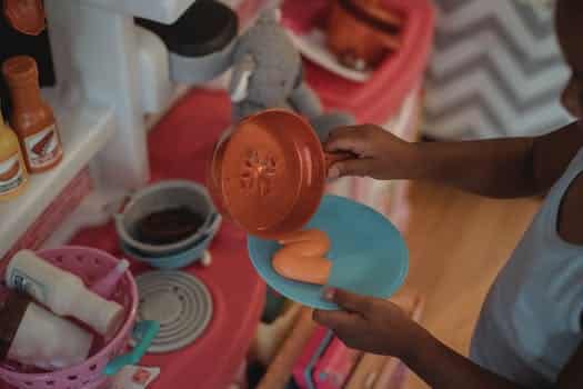 High angle side view of unrecognizable ethnic kid using plastic kitchenware while playing on kitchen