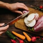 Person Slicing White Onion on Brown Wooden Chopping Board