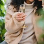 Anonymous female in smart casual clothes with glass of champagne celebrating occasion with friend