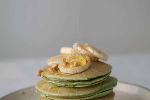 Appetizing sweet pancakes with honey and pieces of fresh banana on gray background