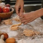 Crop anonymous female chef making homemade Italian pasta nests while cooking in modern kitchen