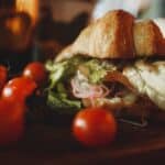 Crunchy veggie croissant sandwich served on board with tomatoes