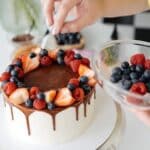 Female confectioner decorating homemade cake with berries