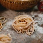 From above nests of fresh homemade uncooked spaghetti placed on wooden table with scattered flour in kitchen