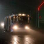 Old trolleybus driving along wet asphalt road in small city at foggy night