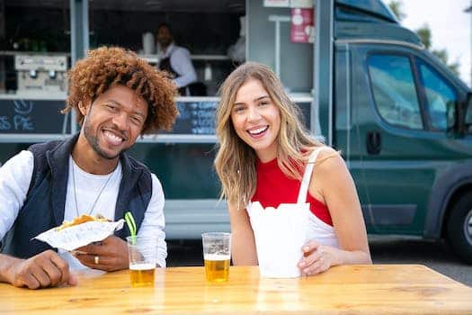 Positive young multiracial friends eating fast food and drinking beer in outdoor cafe