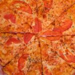 Top view of crop faceless person at table with pizza slices with tomatoes and cheese with seasoning