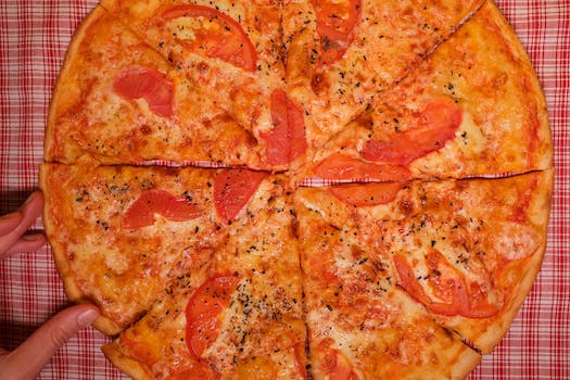 Top view of crop faceless person at table with pizza slices with tomatoes and cheese with seasoning