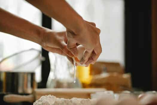 Unrecognizable woman cracking egg into flour on table making dough in kitchen on blurred background