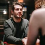 Young man in casual clothes sitting at table in modern cafe with girlfriend