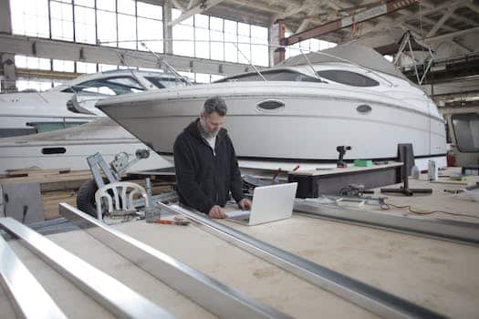 Adult worker using laptop at workbench during work in boat garage