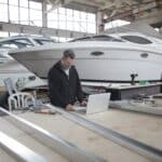 Adult worker using laptop at workbench during work in boat garage