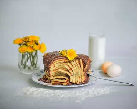 Composition of yummy homemade pancakes topped with chocolate cream placed on white table near glass of fresh milk and glass with yellow flowers