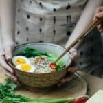 Crop unrecognizable women decorating noodles soup with cut chili pepper