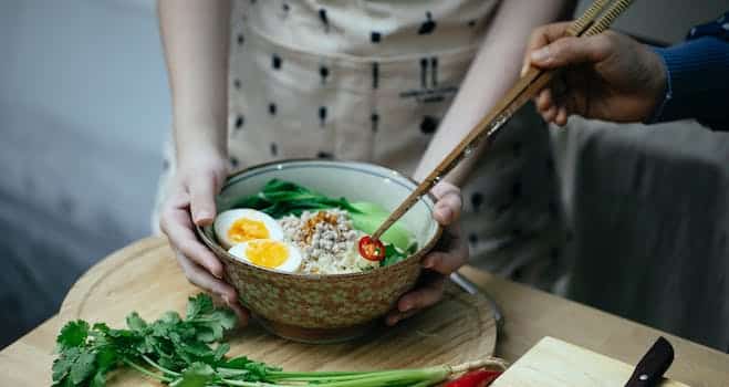 Crop unrecognizable women decorating noodles soup with cut chili pepper