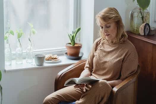 Elderly woman reading textbook against tea and cookies in house