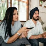 Serious ethnic couple watching movie on sofa