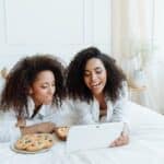 Two Women with Curly Hairs Watching on a Digital Tablet with Snacks