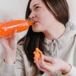 Woman with snack drinking lemonade from plastic bottle